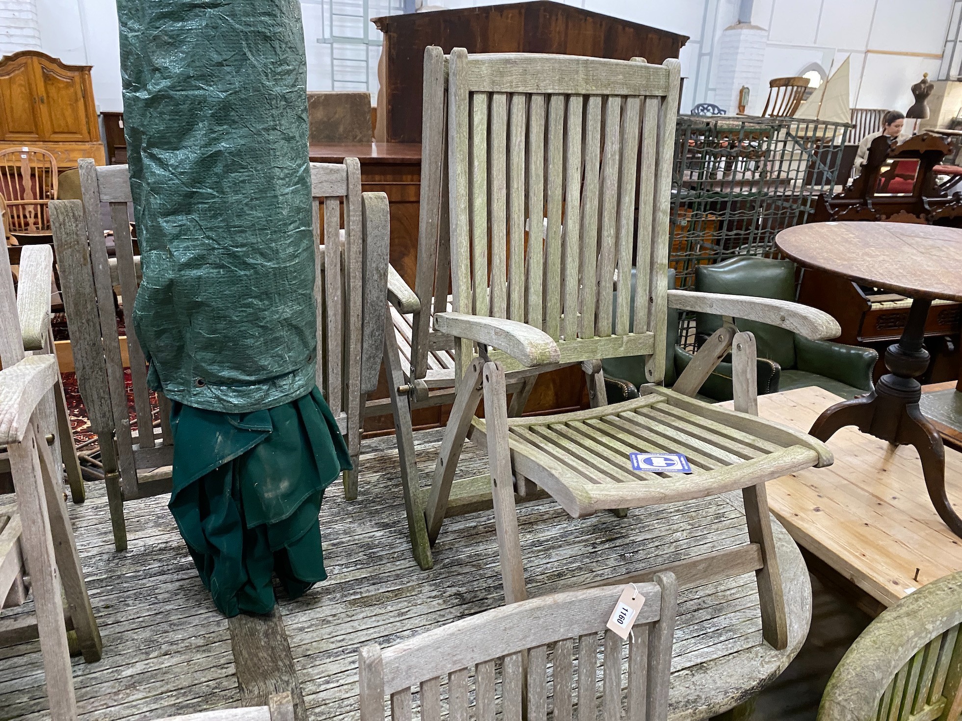 An oval teak garden table, length 260cm, depth 119cm, height 74cm together with eight folding chairs, parasol and cast metal stand.